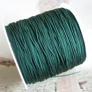 May include: A spool of dark green nylon cord. The cord is tightly wound around a white plastic spool. The cord has a smooth, shiny appearance. This cord is suitable for jewellery making, crafting, and other DIY projects.