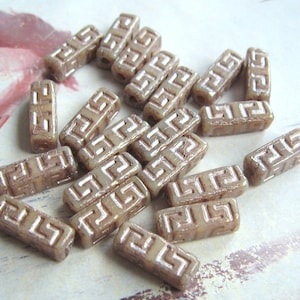 Op de afbeelding: Een verzameling beige glazen kralen met een reliëf geometrisch patroon. De kralen zijn rechthoekig van vorm en hebben een subtiele glans.