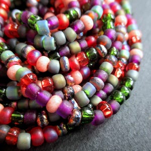 May include: A close-up shot of a collection of colourful glass beads in shades of red, green, purple, and blue. The beads are strung together, creating a textured and vibrant display. The beads are small and round, ideal for jewellery making.