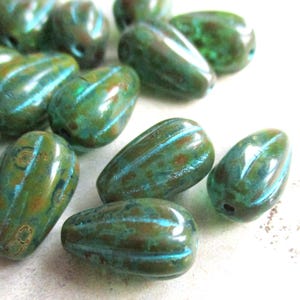 Può includere: Una collezione di perline a forma di goccia nei toni del verde, turchese e marrone. Le perline hanno una finitura lucida e sono decorate con sottili strisce parallele. Ideali per la creazione di gioielli e progetti artigianali.
