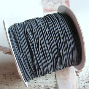 May include: A spool of black elastic cord, wound tightly on a white cardboard spool.