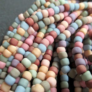 Könnte beinhalten: Nahaufnahme einer Schnur kleiner, matter Glasperlen in verschiedenen Pastellfarben, darunter Rosa, Blau, Grün und Braun.