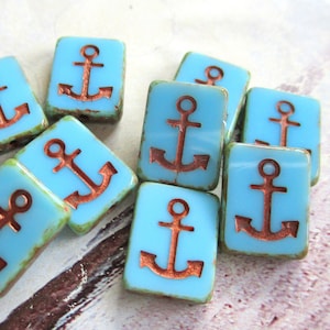 Könnte beinhalten: Eine Sammlung von türkisblauen Keramikfliesen mit Ankermotiven aus Kupfer. Die Fliesen sind quadratisch und haben einen leicht abgenutzten Look.