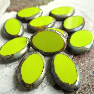 Puede incluir: Una colección de diez cuentas de cerámica de forma ovalada con un esmalte amarillo brillante y un borde metálico plateado.