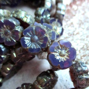 Könnte beinhalten: Eine Reihe von irisierenden Glasperlen mit Blumenmuster. Die Perlen sind eine Mischung aus Lila und Gold.