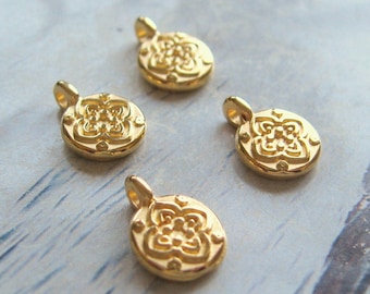 Könnte beinhalten: Vier kleine, goldfarbene Anhänger mit floralem Design. Jeder Anhänger ist rund mit einer Schlaufe oben zum Befestigen an einer Kette oder anderen Schmuckkomponente. Die Anhänger haben ein erhabenes, detailliertes Blumenmuster.