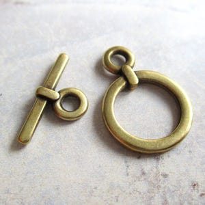 May include: A pair of antique brass toggle clasps, one with a round ring and the other with a straight bar. These clasps are perfect for adding a vintage touch to jewelry or other crafts.