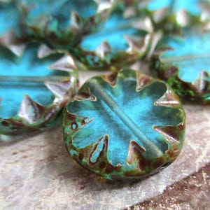 May include: Teal blue glass beads with a brown and green mottled finish. The beads have a starburst design and a hole through the center.