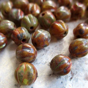 Könnte beinhalten: Eine Sammlung von braunen, grünen und roten Glasperlen mit einer strukturierten Oberfläche. Die Perlen haben eine marmorierte Optik und sind etwa 2,5 cm im Durchmesser.