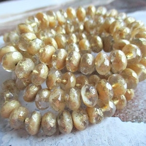 Op de afbeelding: Een streng gouden en heldere glazen kralen met een gefacetteerde, afgeronde vorm. De kralen hebben een metallic glans en zijn geregen op een doorzichtige draad.