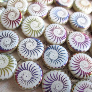 Könnte beinhalten: Eine Sammlung weißer, runder Glasperlen mit einem Spiralmuster in verschiedenen Farben, darunter Lila, Blau und Grün. Die Perlen haben eine glänzende Oberfläche und einen dekorativen Rand. Geeignet für Schmuckherstellung oder Bastelprojekte.