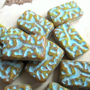 Könnte beinhalten: Eine Sammlung rechteckiger Perlen mit strukturierter Oberfläche. Die Perlen sind hauptsächlich braun und gelb, mit einem türkisfarbenen Muster. Diese Perlen werden wahrscheinlich für die Schmuckherstellung oder andere Bastelprojekte verwendet.