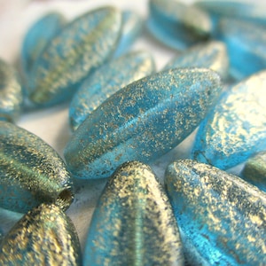 Op de afbeelding: Een close-up van een groep turquoise blauwe glazen kralen met gouden vlokken. De kralen zijn ovaalvormig en hebben een licht getextureerd oppervlak.