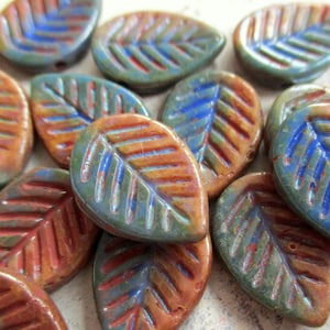 Peut inclure: Une collection de perles en forme de feuille présentant un vernis multicolore avec des nuances de bleu, de vert et d'orange. Chaque perle possède un motif de nervures en relief sur la surface, créant un design de feuille distinctif.