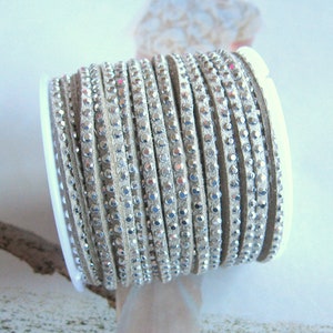 May include: A spool of beige leather cord with silver rhinestones. The cord is wrapped around a white plastic spool.