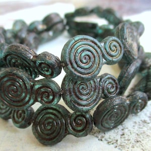 Può includere: Primo piano di un braccialetto con perline a spirale verde-blu scuro. Le perline hanno un aspetto strutturato e invecchiato con accenti dorati. Il braccialetto è probabilmente fatto a mano.