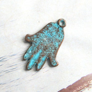 May include: A turquoise blue and brown metal charm in the shape of a hamsa hand. The charm has a distressed finish and a small loop at the top for attaching to a necklace or bracelet.