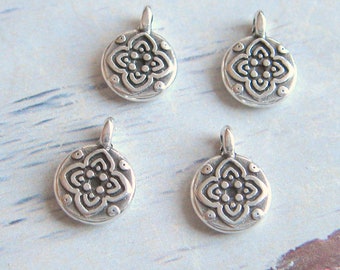 Könnte beinhalten: Vier silberfarbene Metall-Anhänger mit floralem Design. Jeder Anhänger hat eine Öse oben zum Anbringen an eine Halskette oder ein Armband.