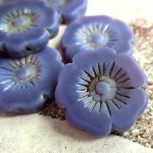 Könnte beinhalten: Eine Gruppe von sechs lilafarbenen Glasperlen in Blumenform mit einem erhabenen Design in der Mitte. Die Perlen haben eine leicht irisierende Oberfläche.