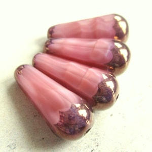 Può includere: Quattro perline di vetro rosa a forma di goccia. Le perline hanno un cappuccio in bronzo metallizzato sull'estremità arrotondata. Il vetro rosa ha un aspetto marmorizzato. Queste perline sono adatte per la creazione di gioielli e l'artigianato.