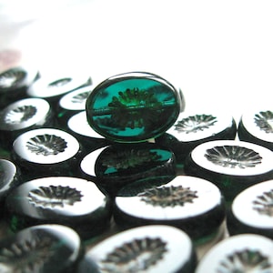 Könnte beinhalten: Nahaufnahme einer Gruppe dunkelgrüner Glasperlen mit floralem Muster. Die Perlen sind oval geformt und haben eine glänzende Oberfläche.