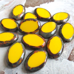 Puede incluir: Una colección de cuentas de cerámica de forma ovalada con un esmalte amarillo y un patrón moteado marrón oscuro y gris.