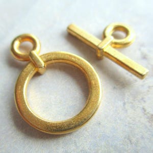 Könnte beinhalten: Goldfarbener Metall-Schiebeverschluss mit einem runden Ring und einer Stange. Der Verschluss ist eine beliebte Wahl für die Schmuckherstellung und das Basteln.