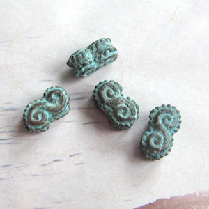Puede incluir: Cuatro cuentas de metal verde azulado con un diseño intrincado. Las cuentas tienen forma de ocho.