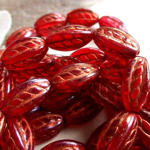 Könnte beinhalten: Nahaufnahme einer Ansammlung von durchscheinenden, roten, ovalen Perlen. Jede Perle hat ein detailliertes, blattartiges Muster in einer kontrastierenden Goldfarbe. Die Perlen sind eng beieinander, was ihre glänzende Oberfläche zeigt.