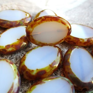 Puede incluir: Un grupo de cuentas de vidrio de forma ovalada con un centro blanco opaco y un borde exterior moteado marrón y amarillo.