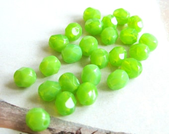 May include: A collection of lime green faceted glass beads. The beads are small and have a slightly translucent appearance.
