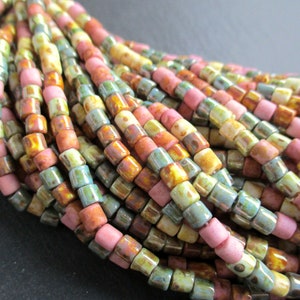 Może przedstawiać: Szereg kolorowych koralików ceramicznych w odcieniach różowego, żółtego, zielonego i brązowego. Koraliki są małe i mają lekko nieregularny kształt.