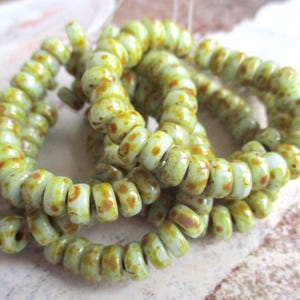 May include: A strand of light green glass beads with brown speckles. The beads are small and round, and they are strung together in a long strand.