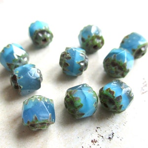 May include: Ten teal blue glass beads with a faceted, starburst design. The beads have a mottled, green and brown pattern throughout.