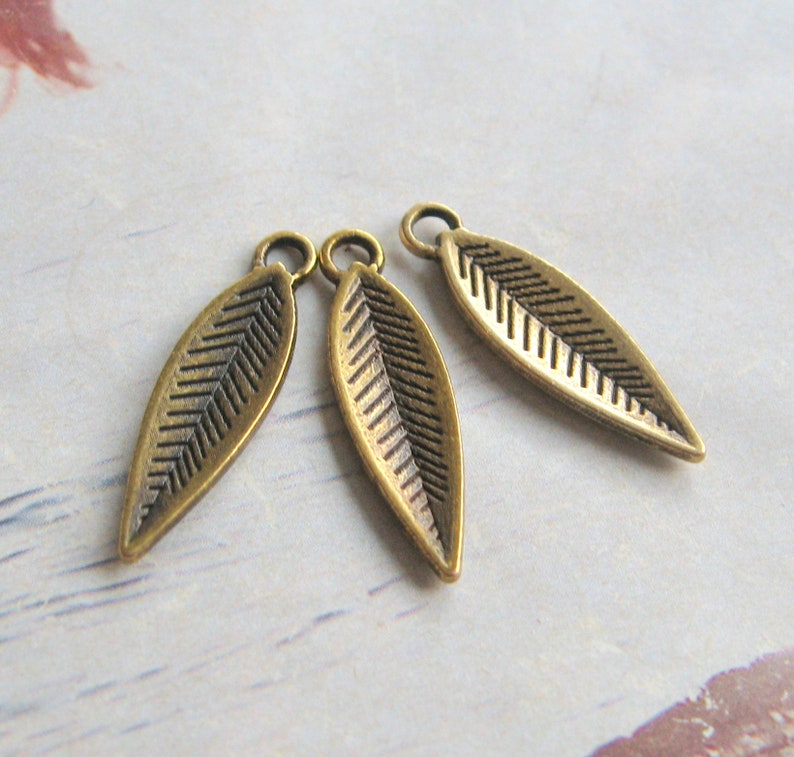 K&ouml;nnte beinhalten: Drei antike goldene Blatt-Anh&auml;nger mit strukturiertem Design. Die Bl&auml;tter sind etwa 2,5 cm lang und haben oben ein Loch zum Anbringen an Schmuck oder andere Bastelarbeiten.