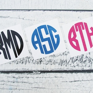 May include: Three circular vinyl decals featuring custom monograms. The first is black with the letters RMD, the second is blue with ASG, and the third is hot pink with BTH. Each decal is presented on a square white backing sheet.