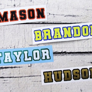 May include: Four personalized name stickers with a sports theme. The names are Mason, Brandon, Taylor, and Hudson. The stickers are on a white wood background.