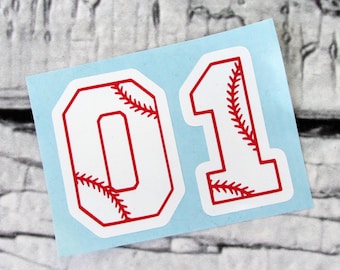 May include: Two white baseball jersey numbers, 0 and 1, with red stitching. The numbers are on a light blue background.