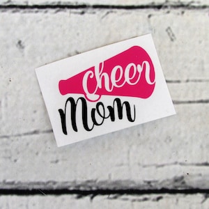 May include: A white sticker with a pink megaphone and the words "cheer mom" in black cursive writing.