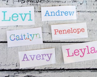 May include: Six rectangular white adhesive labels featuring custom names printed in various colors and fonts. The names include Levi in teal, Andrew in light blue, Caitlyn in a multicolored pattern, Penelope in red, Avery in lavender, and Leyla in pink.