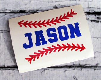 May include: A white sticker with the name "JASON" in bold blue letters, framed by red baseball stitching. The design is reminiscent of a baseball. The sticker is on a light-colored surface.