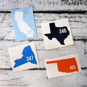May include: Four stickers featuring state outlines with area codes. California is light blue with "323", Texas is black with "346", New York is blue with "347", and Oklahoma is orange with "405".