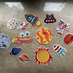 Puede incluir: Un conjunto de 12 parches para planchar con temática espacial. Los parches son coloridos e incluyen imágenes de planetas, cohetes, astronautas y naves espaciales.