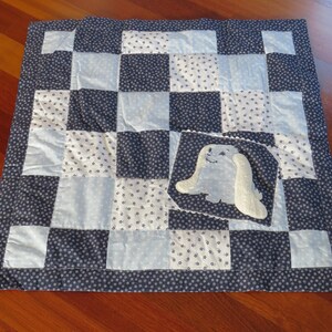 Könnte beinhalten: Eine blaue und weiße Patchwork-Babydecke mit einer blauen Hasenapplikation in der Mitte.