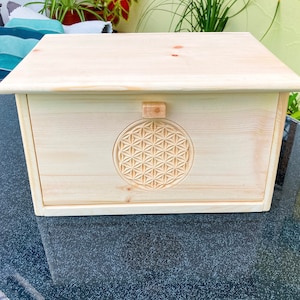 Könnte beinhalten: Eine Brotbox aus Holz mit einem geschnitzten Lebensblume-Design auf der Vorderseite. Die Box ist aus hellem Holz gefertigt und hat ein schlichtes, natürliches Aussehen.