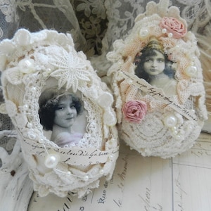 May include: Two off-white, crocheted baby shoes with vintage portraits inside. The shoes are adorned with lace, pearls, and small fabric roses. One shoe has a large, white, lace flower on top.