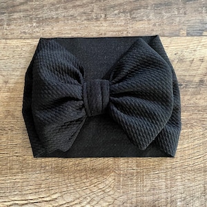 May include: Black fabric headband with a large, black bow. The headband is made of a soft, stretchy material and is perfect for adding a touch of style to any outfit.
