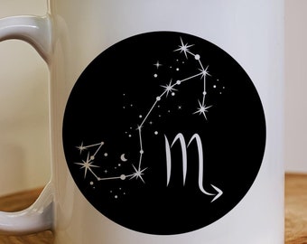 May include: White ceramic mug with a black circle design featuring a constellation of stars in the shape of the zodiac sign Scorpio. The constellation is outlined in white and the sign is in black.