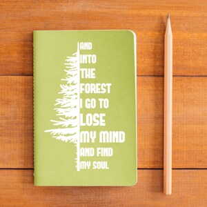 Puede incluir: Una libreta verde con un dise&ntilde;o de &aacute;rbol blanco y el texto "And into the forest I go to lose my mind and find my soul".
