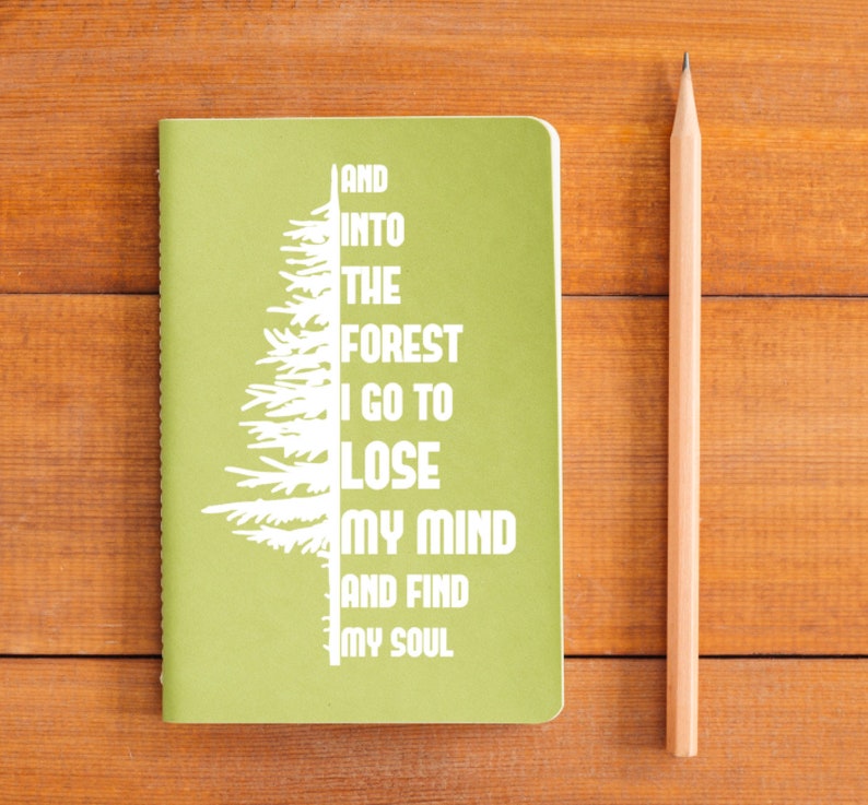 Puede incluir: Una libreta verde con un dise&ntilde;o de &aacute;rbol blanco y el texto "And into the forest I go to lose my mind and find my soul".